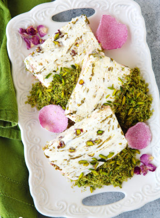 A show stopping ice cream cake with the much-loved flavors of the Middle East!  Scented eshta no-churn ice cream with nibs of caramelized pistachios, swirls of pistachio butter and a crown of green pistachio kunafa on top.  It is a pistachio lover dream come true and much easier to make than it seems.  Plus...recipe VIDEO at the end of the post!